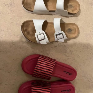 Två par sandaler, vita & rosa Fashion - Säljer två par sandaler! Ett par vita sandaler med två breda remmar och silvriga spännen, klassisk korksula. Det andra paret är rosa slides från Fashion med svartprickigt mönster på remmen. Perfekta för sommaren och chill dagar.