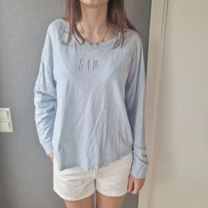 Ljusblå långärmad tröja från GAP - Ljusblå långärmad tröja från GAP med avslappnad passform och rund halsringning. Tröjan är i tunn bomull och har tryckt logga framtill. Perfekt för vår och sommar när du vill ha något enkelt och snyggt.