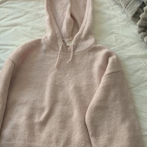 Ljusrosa stickad hoodie från Gina Tricot - Supermjuk och mysig ljusrosa stickad hoodie från Gina Tricot. Tröjan har huva med snörning och långa ärmar. Perfekt för kyliga dagar när du vill vara både bekväm och snygg.