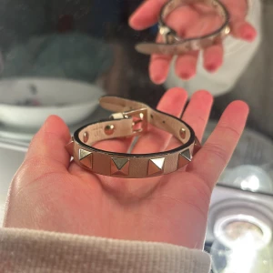 Valentino armband  - Snyggt beige armband i läder med coola pyramidformade nitar i silverfärg. Justerbart spänne och svart kant runt om ger en edgy vibe. Perfekt accessoar för att lyfta din outfit med lite extra attityd. Dustbag och box tillkommer skicka för fler bilder❤️