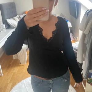 Svart långärmad topp med spets Vero Moda - Svart långärmad topp från Vero Moda med v-ringning och snygga spetsdetaljer längs urringningen. Toppen är lite kortare vid magen och sitter tajtare under bysten. Materialet är sammets liknande som är väldigt mjuk och skönt. Endast använd en gång☺️