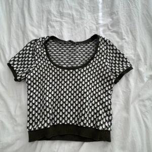 Svartvit rutig croppad topp - Snygg croppad topp med svartvitt rutigt mönster och ribbade kanter. Rund halsringning och korta ärmar ger en trendig vibe. Perfekt att styla med höga jeans eller kjol för en cool look.