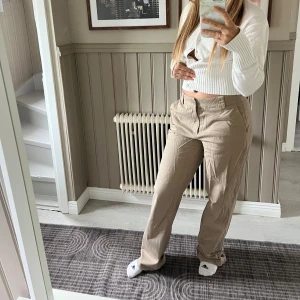 Beiga chinos med raka ben - Säljer ett par snygga beiga chinos med raka ben och normal passform. Byxorna har klassiska fickor fram och bak, bälteshällor och stängs med dragkedja och knapp. Perfekta för en clean och avslappnad look.