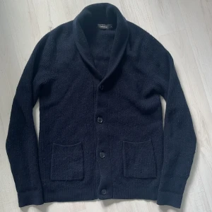 Mörkblå stickad kofta med sjalkrage - Säljer min mörkblå kofta /cardigan ifrån Dressman. Perfekt att slänga på sig över en t-shirt och grym kvalité. Skick 9/10 använd men utan någon defekt!🙌Kom gärna med prisförslag!