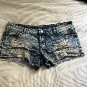 Low waist jeans shorts - Snygga blå jeansshorts från Amisu med slitna detaljer, pärlor och råa kanter. Shortsen har klassisk femficksmodell, låg midja och cool tvättad look. Perfekta för sommaren när du vill ha en edgy stil.