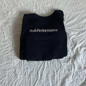 Svart sweatshirt från Peak Performance - Svart sweatshirt från Peak Performance med vit logga framtill. Klassisk rund halsringning och långa ärmar. Mjuk insida och ribbade muddar vid ärmslut och nederkant. Perfekt för en clean och sportig look. Det är storlek M men känns som S