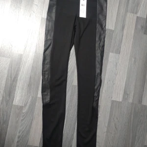 Svarta leggings från Vero Moda S - Svarta leggings från Vero Moda i storlek S. Byxorna har snygga skinnliknande paneler längs sidorna som ger en cool kontrast till det matta tyget.