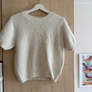 Vit stickad tröja från Gina Tricot - Supermysig vit stickad tröja från Gina Tricot med korta ärmar och ribbade muddar. Perfekt för lager-på-lager och chill vibes. Rund halsringning och relaxed fit gör den enkel att styla till jeans eller kjol.