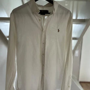 Vit linneskjorta skjorta från Ralph Lauren, slim fit - Klassisk vit skjorta från Ralph Lauren i slim fit-modell. Skjortan har button down-krage, broderad logga på bröstet och är tillverkad i bomull. Perfekt för dig som gillar stilrena och tidlösa plagg med snygg passform.