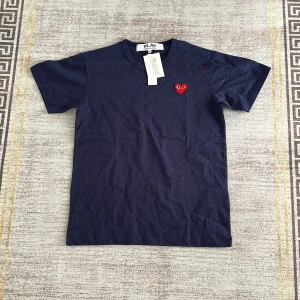 Blå Comme des Garçons Play t-shirt - Mörkblå t-shirt från Comme des Garçons Play med klassiskt rött hjärta med ögon broderat på bröstet. T-shirten har rund halsringning och korta ärmar. Tillverkad i mjuk bomull för en skön känsla och clean look.