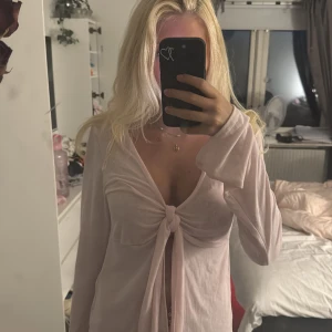 Ljusrosa omlottopp med knyt - Supersöt ljusrosa omlottopp med lång ärm. Toppen har en knyt-detalj framtill. Knappt använd få ja råka köpa i för stor storlek💓