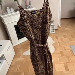 Leopardmönstrad långklänning med bälte - Snygg långklänning från Urban Bliss med leopardmönster och knytbälte i midjan. Klänningen har smala axelband och en loose passform som ger en avslappnad men trendig look. Perfekt för dig som vill sticka ut med ett djurmönster.