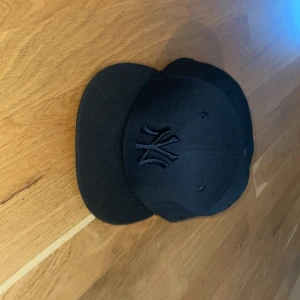 Svart New Era Yankees 59FIFTY keps - Säljer en svart New Era 59FIFTY keps med New York Yankees-logga broderad framtill i svart. Klassisk flat peak och MLB-logga baktill. Kepsen är i modellen fitted och tillverkad i ett slitstarkt material som känns riktigt premium. Storlek 58,7 cm 