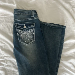 Jeans med broderad fjäril och vita stenar - Mörkblå jeans med snyggt slitna detaljer och vita sömmar. Bakfickan har en stor broderad fjäril i vitt med glittriga stenar som ger extra bling. Det är storlek M men jag skulle säga att det är mer som S, byxorna är midwaist men super sköna och fina. Det finns ingen lapp vart dom är ifrån eller storlek och jag kommer tyvärr inte ihåg vart jag köpte dom. Inte använt särskilt många gånger eftersom att dom var lite för småa! Snabb affär 220kr🩷