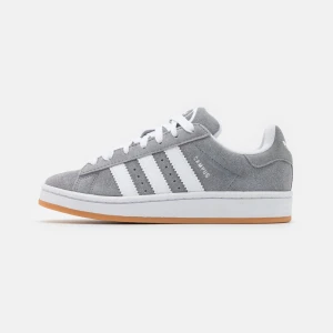 Adidas Campus grå sneakers mocka - Grå Adidas Campus sneakers i mocka med klassiska vita ränder på sidorna och vit sula med gummidetalj. Skorna har snörning och låg profil, perfekt för en clean och stilren look. Jättebra skick.