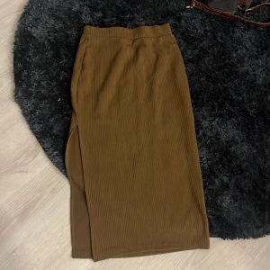 Brun ribbad långkjol med slits - Snygg brun långkjol i ribbat material med en stilren slits på sidan. Kjolen har en rak passform och resår i midjan för extra komfort. Perfekt att styla med chunky sneakers eller boots.