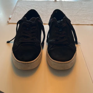 Svarta mockasneakers med vit sula - Svarta sneakers i mocka med klassisk låg profil och vit platt sula. Skorna har rund tå, svarta snören och en stilren look som passar till det mesta. Perfekta för dig som gillar en enkel men snygg stil.
