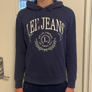 Mörkblå hoodie från Lee Jeans - Snygg mörkblå hoodie från Lee Jeans med stor vit logga framtill, riktigt snyggt tryck. Perfekt för chill dagar eller när du vill ha en avslappnad look. Använd men i fint skick. Hör av er vid frågor