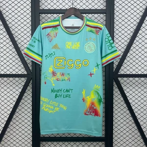 Ajax x Adidas Bob Marley fotbollströja - Unik ljusblå Ajax fotbollströja från Adidas med Bob Marley-inspirerade tryck, färgglada detaljer i rött, gult och grönt samt Ziggo-logga. Kortärmad modell med coola grafiska motiv, citat och klubbmärke på bröstet. Perfekt för dig som vill sticka ut på läktaren eller i stan.