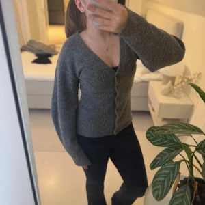 Grå kofta med v-ringning och knappar - Mysig grå kofta med v-ringning och knappar framtill. Modellen är figurnära med långa ärmar och lätt melerad yta. Perfekt att slänga över en topp för en chill look. Materialet känns stickat och är superbekvämt.