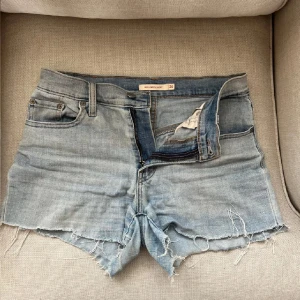 Levi's ljusblå jeansshorts med rå kant - Ljusblå jeansshorts från Levi's med låg midja och rå, fransig kant. Klassisk femficksmodell med Levi's-logga bak och slitna detaljer för en avslappnad vibe. Perfekta till sommaren och lätta att matcha med allt.