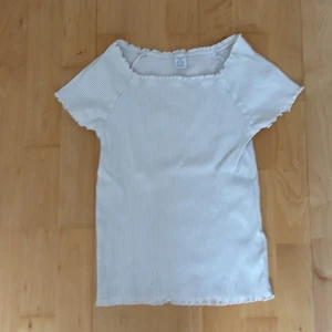 Vit ribbad topp från Lindex - Säljer en söt vit ribbad topp från Lindex i storlek 170. Toppen har korta ärmar, diskreta ränder och volangkant vid hals, ärmslut och nederkant. Perfekt för dig som gillar en enkel men ändå gullig stil.