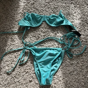 Turkos bikini med snörning - Snygg turkos bikini med bygel och smala axelband. Både överdel och underdel har knytband i sidorna för en justerbar passform. Perfekt för stranden eller poolen, enkel och stilren design i mjukt material. Endast testad/använd 1 gång och tvättad efter det. (Har ej badat med den) Underdelen är storlek S, överdelen är 70B. 20kr för båda delarna.