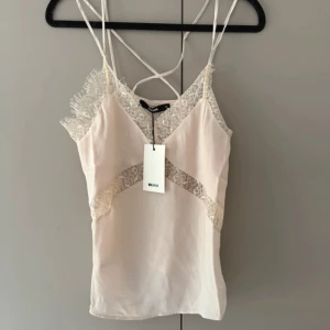 Beige spetslinne från Bik Bok XS - Supersött beige linne från Bik Bok i storlek XS. Tunt tyg med v-ringning, smala axelband och fina spetsdetaljer både upptill och längs sidorna. Perfekt för dig som gillar romantisk och feminin stil. Linnet har en lätt glansig finish och snyggt fall.