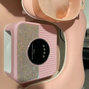 Nagellampa med glitterdetaljer / nageltillbehör/ nail dust collector  - Jag har bestämt mig att sluta med naglar, därför säljer jag alla mina naglar tillbehör, inköpt för över 1000 och säljer för endast 550kr. I detta ingår alla nail dust collector, nagellack förvaring 5 hög, nagel uv lampa,nagel arm cushion, och soak off bowl. Skriv om du är intresserad eller vill prata om priset  Nagellampa i ljusrosa med glittriga detaljer och svart display, perfekt för gelnaglar. Inkluderar även rosa handstöd och skål för manikyr. 