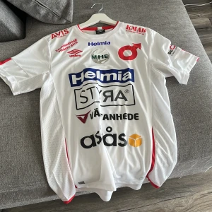 Degerfors match bärd tröja! Med morgados signatur som ni ser på bild 5 storlek M - Säljer en vit fotbollströja från Umbro med röda detaljer och tryck. Tröjan har korta ärmar, flera sponsorloggor på framsidan och spelartryck 'Morgado 30' på ryggen, samt autograf. Tillverkad i lätt och ventilerande polyester. Match bärd