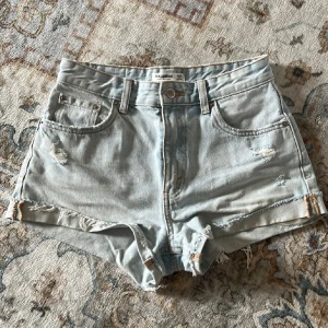 Ljusblå jeansshorts från Pull&Bear - Säljer ett par ljusblåa jeansshorts från Pull&Bear med fransiga kanter, bälteshällor och slitna detaljer framtill och bak. Perfekta för sommaren.