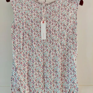 Mönstrad blus från Esprit, vit - Supersöt blus från Esprit i vitt med färgglatt geometriskt mönster i rosa, turkos och lila. Blusen är ärmlös med rund halsringning och har en lätt och luftig känsla, perfekt för varmare dagar. Snygg att matcha med jeans eller kjol!