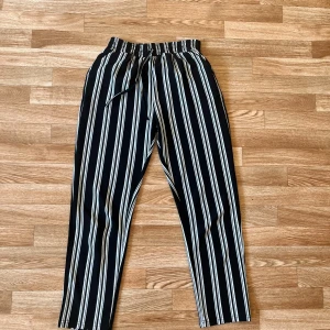 Stretchiga mönstrade byxor  - Svarta byxor med vita vertikala ränder och elastisk midja med snörning. Modellen har raka ben och är tillverkad i ett mjukt, lätt tyg som känns skönt mot huden. 