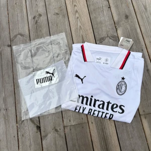 Vit AC Milan fotbollströja Puma - AC Milan bortatröja från Puma i vitt med svarta och röda detaljer på krage och ärmslut. Tröjan har klubbmärke och Puma-logga på bröstet samt sponsortryck framtill. Tillverkad i lätt och ventilerande funktionsmaterial, perfekt för match eller träning. Pris kan diskuteras vid snabb affär 