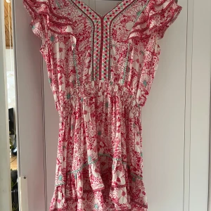 Blommig kortklänning med volang - Supersöt kortklänning med blommigt mönster i rosa, vitt och turkost. Klänningen har volangärmar, smock i midjan och fina detaljer vid halsringningen. Perfekt för sommaren. Köpt för 2000 säljer för 500🥰 från poupette st barth