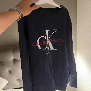 Calvin Klein långärmad – mörkblå, vit logga, stl S - Säljer en stilren långärmad tröja från Calvin Klein i mörkblå färg med klassisk vit CK-logga framtill. ✔️ Äkta vara ✔️ Storlek S ✔️ Mjukt och skönt material ✔️ I mycket bra skick – inga defekter, noppor eller fläckar  Passar perfekt till både vardag och en mer clean outfit.  💬 Hör av dig för fler bilder eller frågor