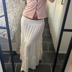 Vit långkjol med volanger - Säljer en superfin vit långkjol med bred resår i midjan och flera volanglager som ger en flowy och luftig känsla. Perfekt för varma dagar och enkel att styla med crop tops eller linnen. Kjolen är helvit och har en romantisk boho-vibe. Går ner till marken på mig som är 162 cm💞 Inte genomskinlig💞