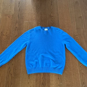 Blå merinoulltröja från CareOfCarl - Snygg blå stickad tröja från Colorful Standard i återvunnen merinoull. Tröjan är i storlek L. Klassisk rund halsringning, ribbade muddar och lång ärm. Perfekt för dig som gillar färg och vill ha något mjukt och bekvämt i garderoben. Köpt på CareOfCarl. Endast använd ett fåtal gånger och finns inga tecken på användning.