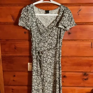 Blommig klänning från Lindex XS - Supersöt svartvit omlottklänning från Lindex i storlek XS. Klänningen har korta ärmar, v-ringning och knyt i midjan. Tunt och skönt material med blommigt mönster, perfekt för vår och sommar. Bara använd ett fåtal gånger.