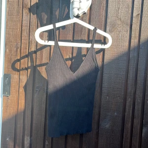 Svart ribbad linnetopp med v-ringning - En svart ribbad linnetopp med smala axelband och djup v-ringning. Toppen är figurnära och har en enkel, stilren look som passar perfekt till jeans eller kjol. Materialet är stretchigt och bekvämt för varma dagar.