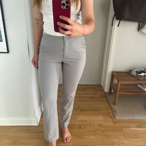 Grå kostymbyxor från H&M, strl 36 - Snygga ljusgrå kostymbyxor från H&M i storlek 36. Byxorna har hög midja, raka ben och klassisk passform. Perfekta till vardags eller fest!