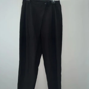 Svarta kostymbyxor med hög midja - Stilrena svarta kostymbyxor med hög midja och klassisk rak passform. Byxorna har knäppning med knapp och dragkedja samt hällor för bälte. Perfekta för en clean och dressad look.