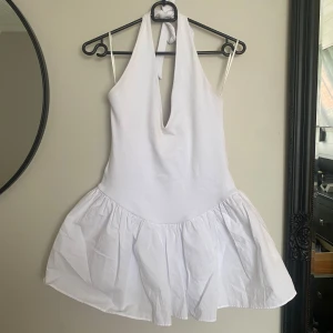 Vit halterneckklänning från Zara - Supersöt vit kortklänning från Zara med halterneck och djup v-ringning. Kjolen är voluminös och har en lätt rynkad effekt. Perfekt för sommarens alla tillfällen när du vill sticka ut lite extra.