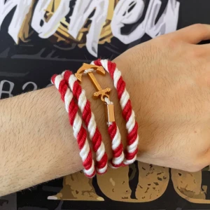 armband - Snyggt armband i tvinnat rött och vitt rep med ett guldigt ankare som lås. Perfekt accessoar för dig som gillar marina vibes och vill sticka ut med något unikt. Armbandet lindas flera varv runt handleden och har coola detaljer i metall.