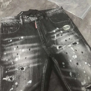 Svarta Dsquared2 jeans med färgstänk - Riktigt snygga svarta jeans från Dsquared2 med slitna detaljer och vita färgstänk över hela byxan. Modellen är slim och har klassisk femficksdesign, Dsquared2-logga på fickan och coolt tvättad finish. Perfekta för dig som gillar streetstyle och vill sticka ut.