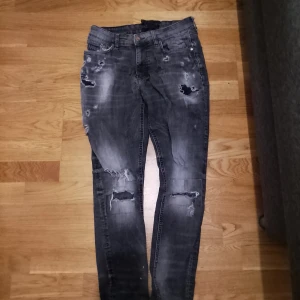 Mörkgrå slitna skinny jeans - Säljer ett par mörkgrå skinny jeans med coola slitningar och hål på både fram- och baksida. Jeansen har klassisk femficksdesign och är tillverkade i stretchigt denim för en tight passform. Perfekta för dig som gillar en edgy streetstil.
