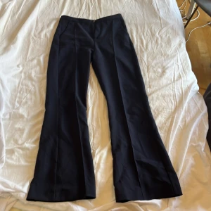 Marinblå bootcut kostymbyxor - Snygga svarta kostymbyxor med vida ben och pressveck. Byxorna har hög midja och stängs med dragkedja fram. Perfekta för en clean och stilren look, passar till både sneakers och boots.