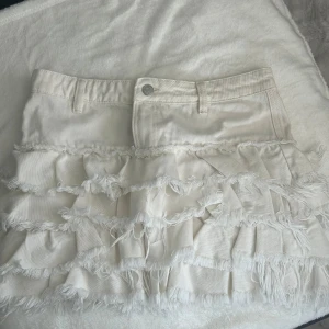 Vit kortkjol med volanger (monki)  - Supersöt vit kortkjol med flera lager volanger och fransiga detaljer. Aldrig använd, storlek 34 kjolen är ifrån monki 
