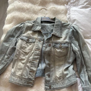 Ljusblå jeansjacka från Penian - Snygg ljusblå jeansjacka från Penian i klassisk modell med krage, bröstfickor med knappar och markerade sömmar. Jackan har långa ärmar och en croppad passform som ger en cool vibe till din outfit. Perfekt att slänga över en hoodie eller t-shirt.