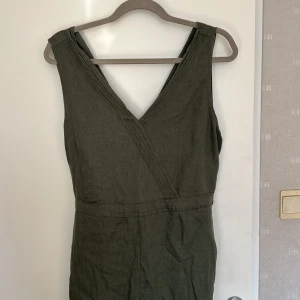Mörkgrön jumpsuit med knyt stl M - Snygg olivgrön ärmlös jumpsuit med omlott-v-ringning och knytband i midjan. Har fickor bak och vid sidan. Perfekt för dig som gillar en chill look. Den är aldrig använd